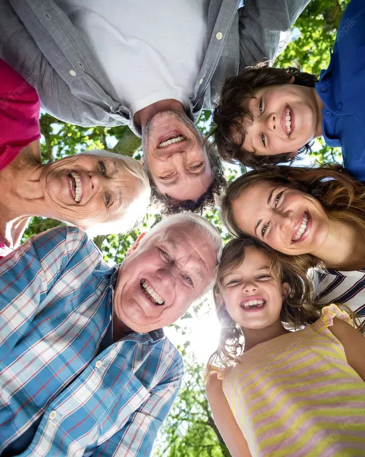 Smiling multigenerational family with heads together in a circle outdoors under green trees